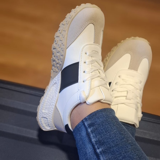 Zapatilla blanca urbana para mujer en color blanco con una franja lateral negra, puntera reforzada en gamuza gris y una distintiva suela de goma color crema con textura de relieve.